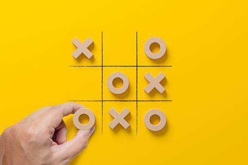 Business marketing strategy planning concept. Hand holding wooden block tic tac toe board game on yellow background
