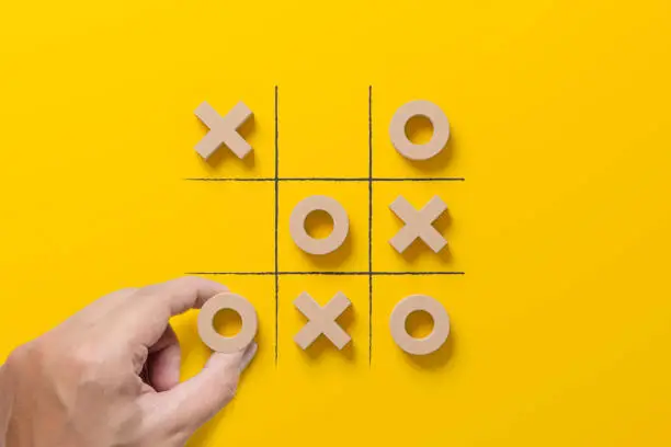 Photo of Business marketing strategy planning concept. Hand holding wooden block tic tac toe board game on yellow background