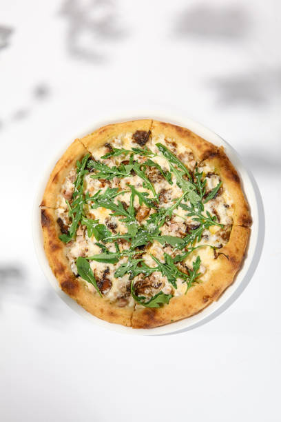 istock Mushroom pizza with cheese and arugula on white background with shadows. Italian pizza with porcini mushrooms on white table and hard shadows Cheese pizza in trendy style. Modern italian food 1443731229