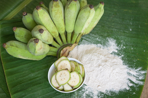 banana powder on bowl and raw banana - banana fruit on leaf background, alternative flour, homemade green banana flour for herbal medicine nature herb
