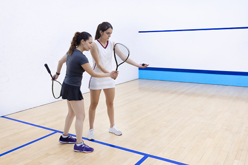 Coach instructing his apprentice on how to pick up the racquet and ball to serve.