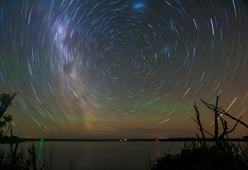 A long exposure reveals the earth's rotation. Stars appear as trails in the sky and are reflected in the lake below.