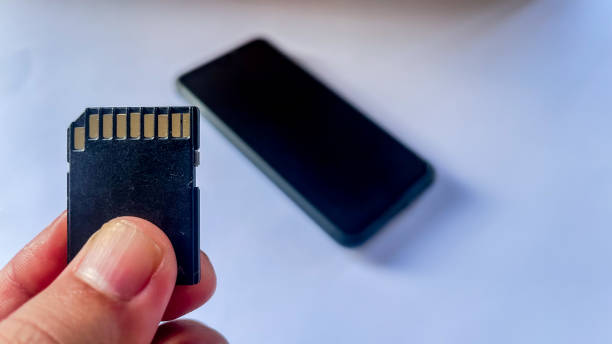 istock Hand holding sdcard isolated on white background with the smartphone blurred on it 1443751882
