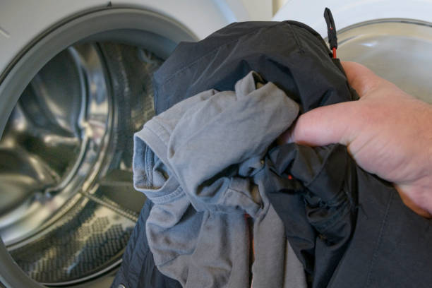 istock Man's hand folds clothes into an open washing machine. Washing dark clothes. 1443753521
