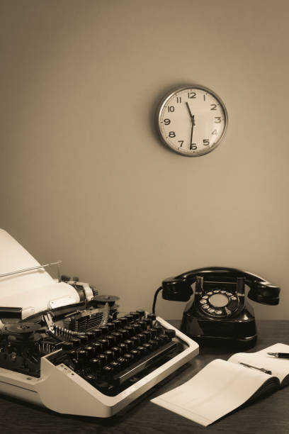 istock A retro typewriter and an old telephone are on the table, along with a checkbook and an ink pen. clock on wall. black and white 1443753526