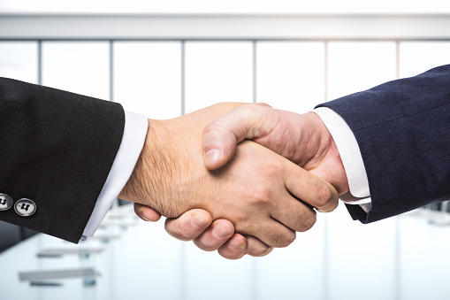 Two business people shaking hand for a deal in office.