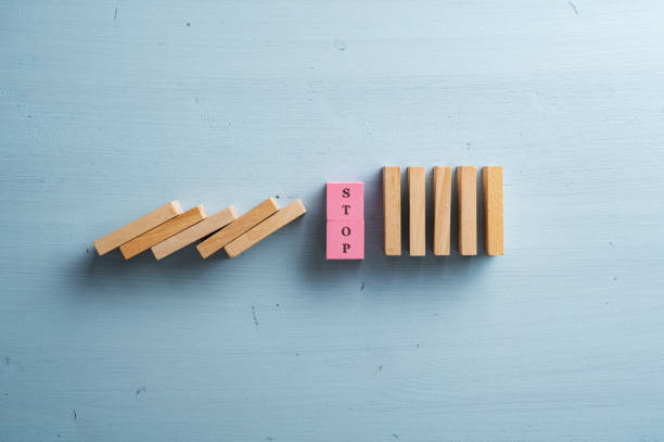 istock Word stop on a stack of pink wooden blocks interrupting collapsing dominos 1443762287