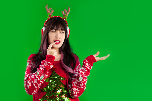 Asian woman long hairstyle wear red sweater earmuffs and reindeer horns headband posing hand pointing green screen background.
