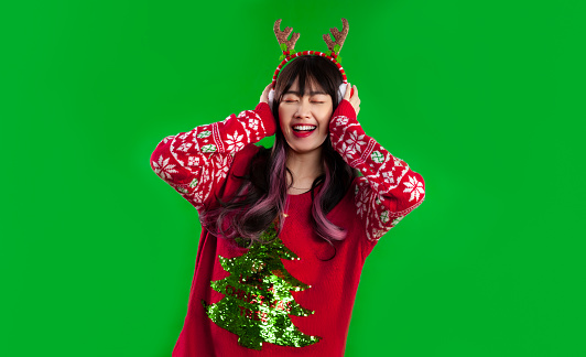 Asian woman long hairstyle wear red sweater happy face listenting to music on green screen background. Merry Christmas concept.