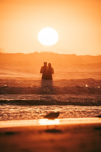 A vertical shot of a couple in the sea during sunset