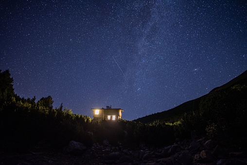 A small illuminated cottage in mountains at starry night