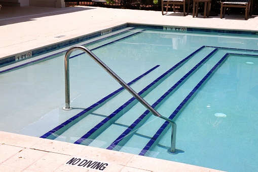The metal handrail with stairs at the pool with clean cold water. Text: no diving.