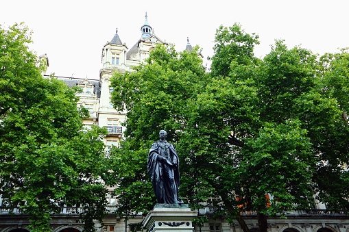 The William Tyndale Statue covered by lush green trees at London Whitehall Gardens