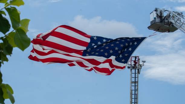 istock Huge waving American flag hanging from construction crane against blue cloudy sky 1443779377