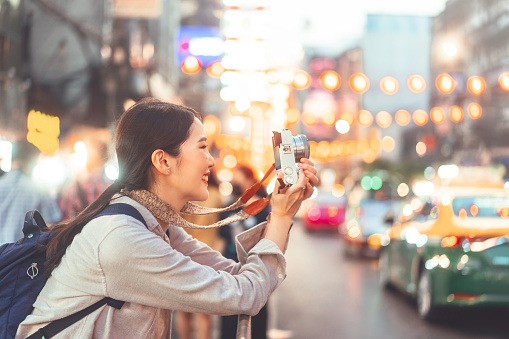 Young adult asian woman traveller backpack using camera photography. People traveling in city lifestyle chinatown street food market Bangkok, Thailand. Staycation southeast asia summer trip concept.