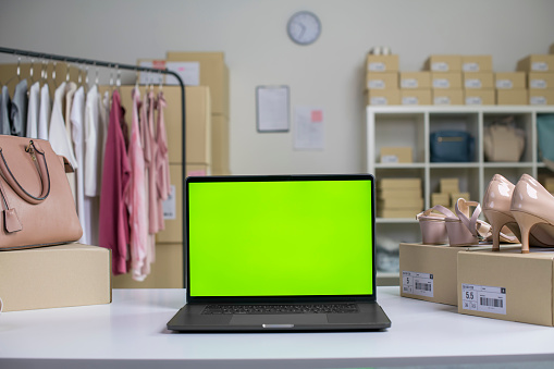 Laptop with blank green screen standing on the desktop in the warehouses. Asian woman online seller checking stock and Inventory before sending to the customer.
