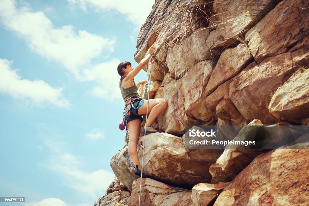 A woman in nature rock climbing, training and fitness outdoors on a sunny day with climbing equipment. A female, strong and healthy athlete doing exercise, physical activity and extreme climbing. Rock Climbing Stock Photo