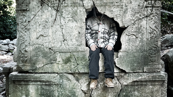 A young man sitting inside an old and destroyed rock tomb.