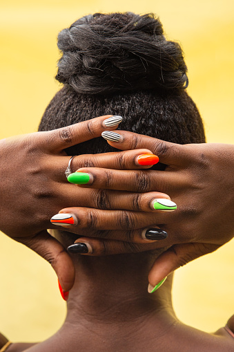 Close up of a young African woman's painted nails put on the back of her head.
