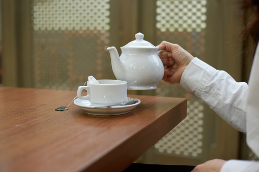A girl pours tea into a mug while sitting at a table tea ceremony.