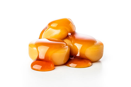 Front closeup view of a three caramel candies dripping caramel sauce isolated on white background