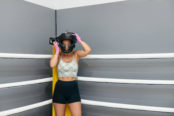 mujer joven poniendo casco protector para practicar boxeo de pie en el ring boxeo - boxing womens fotografías e imágenes de stock