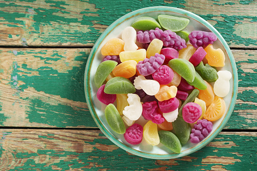 Mix of fruits gummy candies on a plate on old green wooden background, top view with copy space