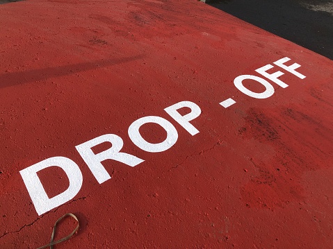 Drop off pick up point parking space sign on red asphalt tarmac in large white letters