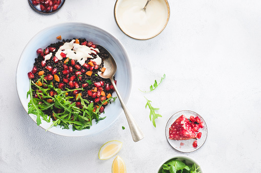 Plant based diet: healthy superfood, black lentil vegan salad with arugula, parsley herb and pomegranate with tahini and lemon dressing. Healthy vegan salad recipe concept, copy space