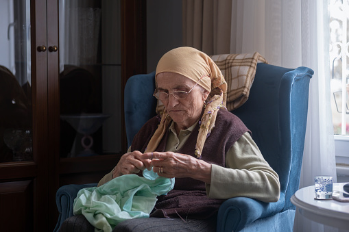 Portrait of an elderly woman crocheting at home.