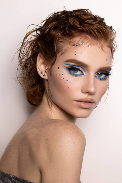 Woman with shimmering skin gently touches her face under a blue light, beauty makeup face