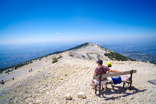 Bedoin, France - August 7, 2022:  People sitting on a weathered bench. At 1,909 m (6,263 ft), it is the highest mountain in the region and has been nicknamed the Beast of Provence.