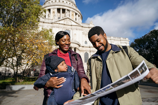 Front view of Black man and woman in mid 20s with 4 month old baby standing outside St. Paul’s Cathedral and planning further sightseeing.