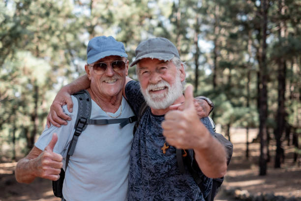 istock Happy smiling couple of elderly men with hat and backpack look in camera with thumbs up while enjoying mountain hike appreciating leisure and freedom, retired seniors and healthy lifestyle concept 1443820337