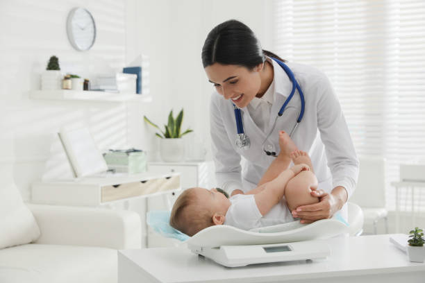 Young pediatrician weighting cute little baby in clinic stock photo