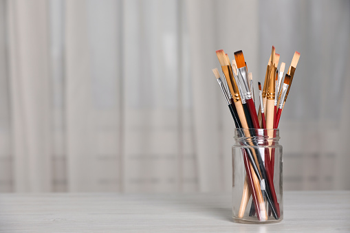 Many different paintbrushes on white wooden table indoors, space for text