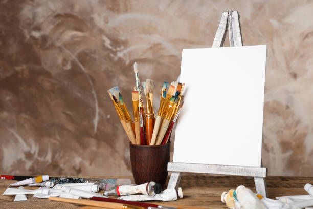 istock Many brushes, easel with blank canvas and paints on wooden table 1443824063