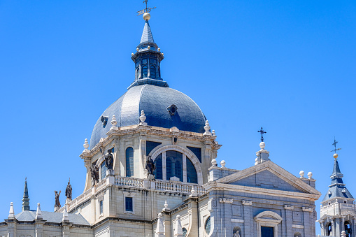 Madrid, Spain - July 19, 2022: Almudena Cathedral. The upper facade of a church. The church has a dome and some tower-like structures with crosses at the top.