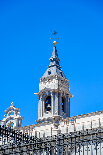 Madrid, Spain - July 19, 2022: Almudena Cathedral. Bell tower on a church building against a blue sky background. The building has a metal fence, and no people are on the scene.