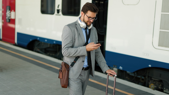 Mid adult businessman with luggage using his smart phone at a railroad station