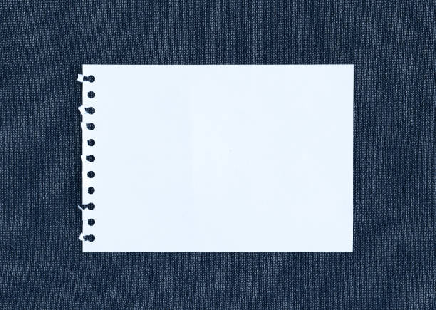 White paper note sheet on fabric background, clothes with label tag, white blank paper on textile background