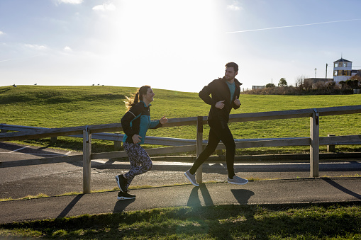 Wide shot of a couple outdoors on a run by the coast in the North East of England. They are completing their New Years resolution to be more active.
