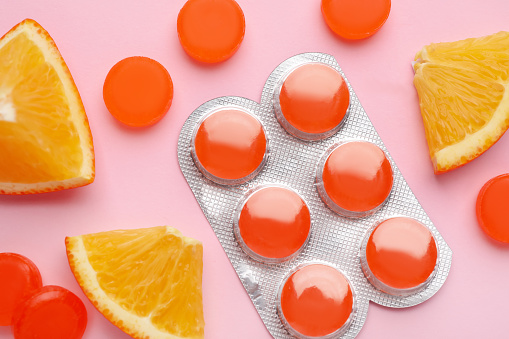 Many orange cough drops on pink background, flat lay