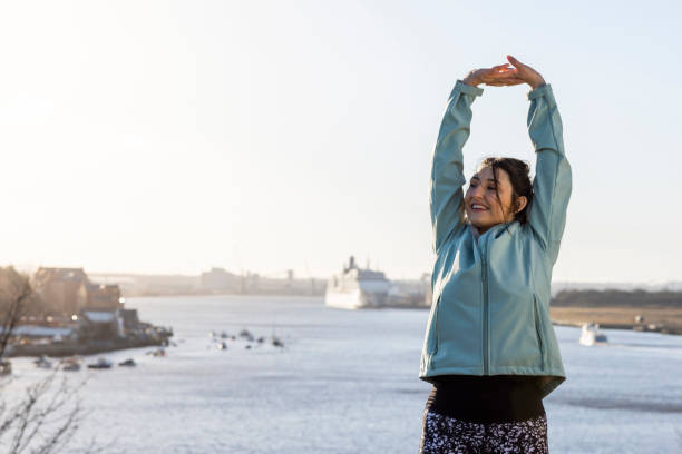 Mindful Exercise in the Morning Woman stretching while out exercising/on a run. She is completing a New Years resolution to be more active. She's on a run by the coast in the North East of England. new year resolution stock pictures, royalty-free photos & images