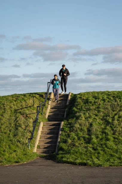 Couple outdoors on a run by the coast in the North East of England. They are completing their New Years resolution to be more active. They are running down stairs in a grass area.