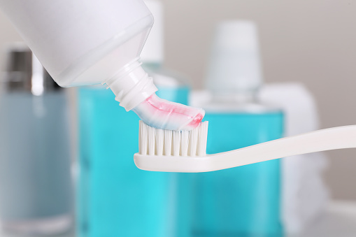 Applying paste on toothbrush near mouthwash, closeup
