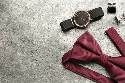 Stylish burgundy bow tie, cufflinks and wristwatch on grey background, flat lay. Space for text