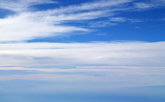 Vivid blue sky and white spreading clouds with an airplane flying in distance view during the flight