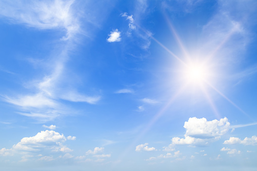 Beautiful, blue summer sky with fluffy clouds and bright sun as a background.