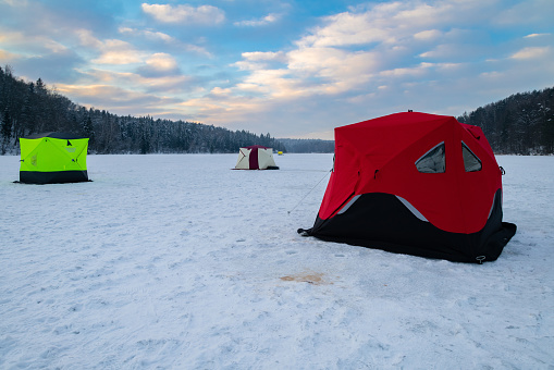 Ice fishing tent on a frozen lake at sunset. Fisherman camp on a peaceful winter evening.